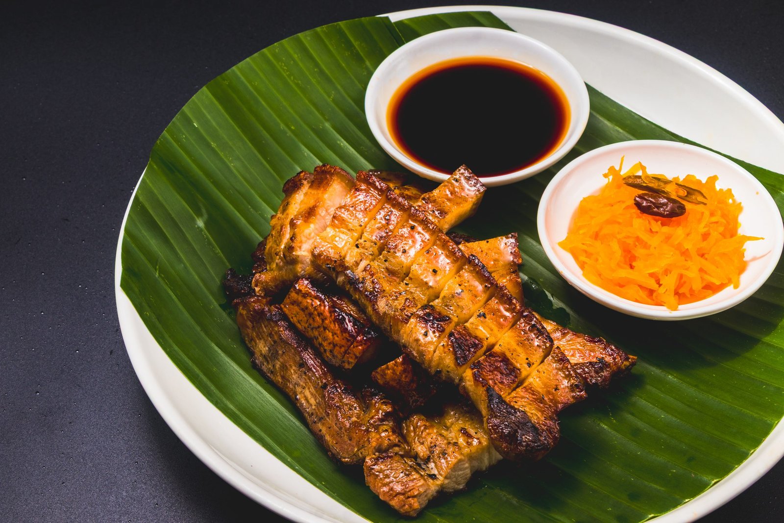 Grilled pork belly on a banana leaf with soy dip and atchara