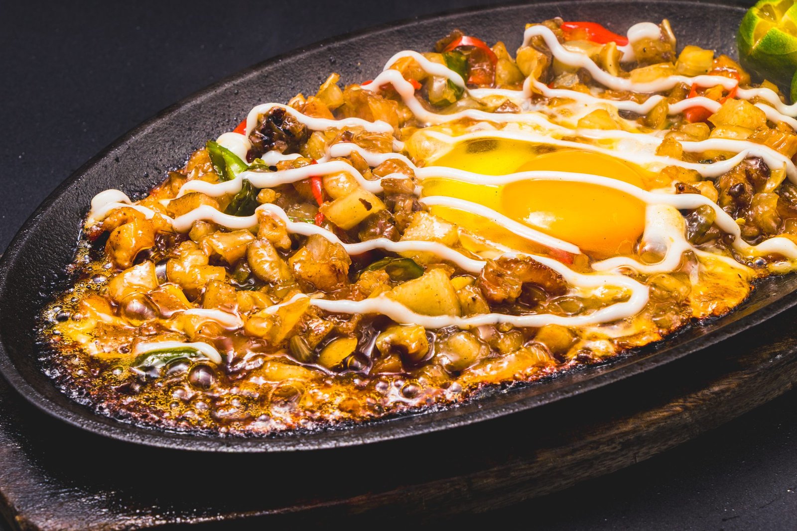 Sizzling pork sisig with egg and calamansi on an iron plate