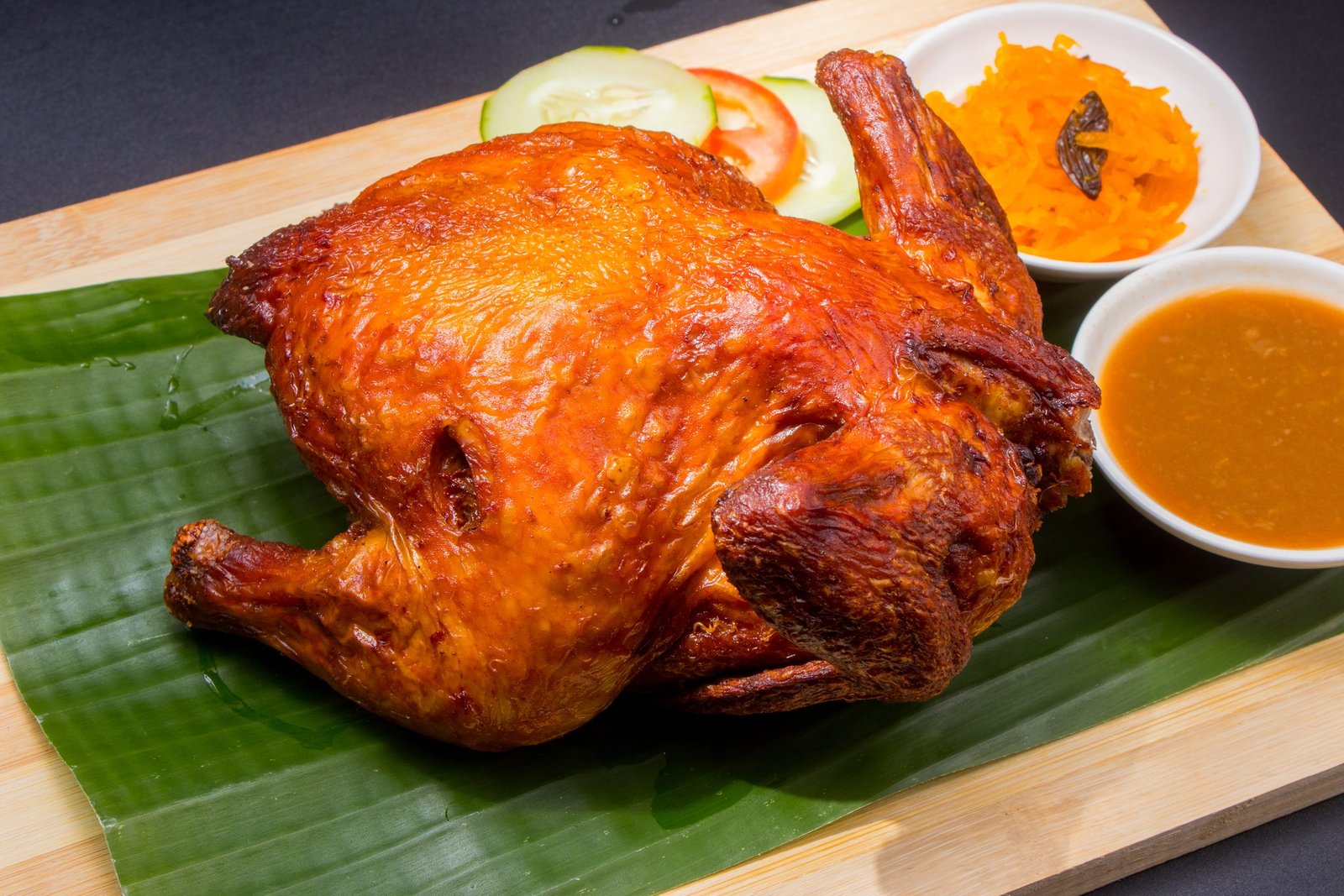 Whole roasted chicken on a banana leaf with sauce and atchara